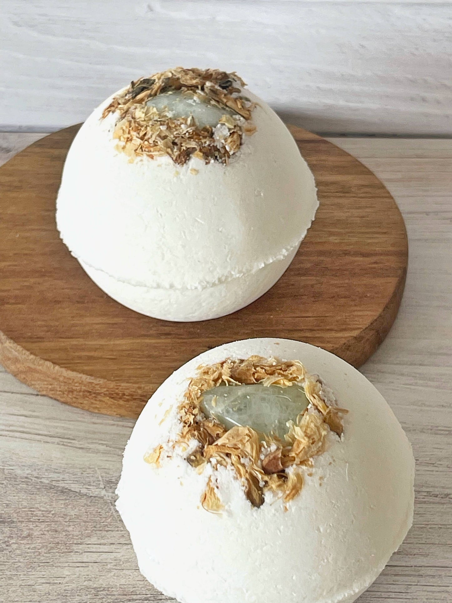 Two white bath bombs with gold flakes on a wooden board.