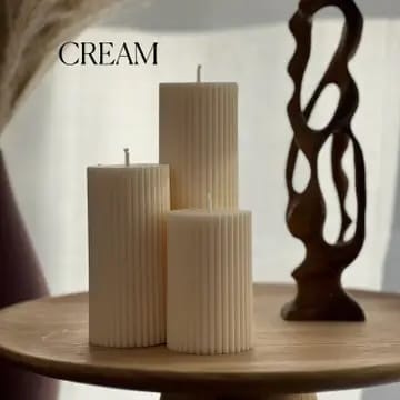 Three ribbed candles on a wooden table with a decorative dark object in the background.