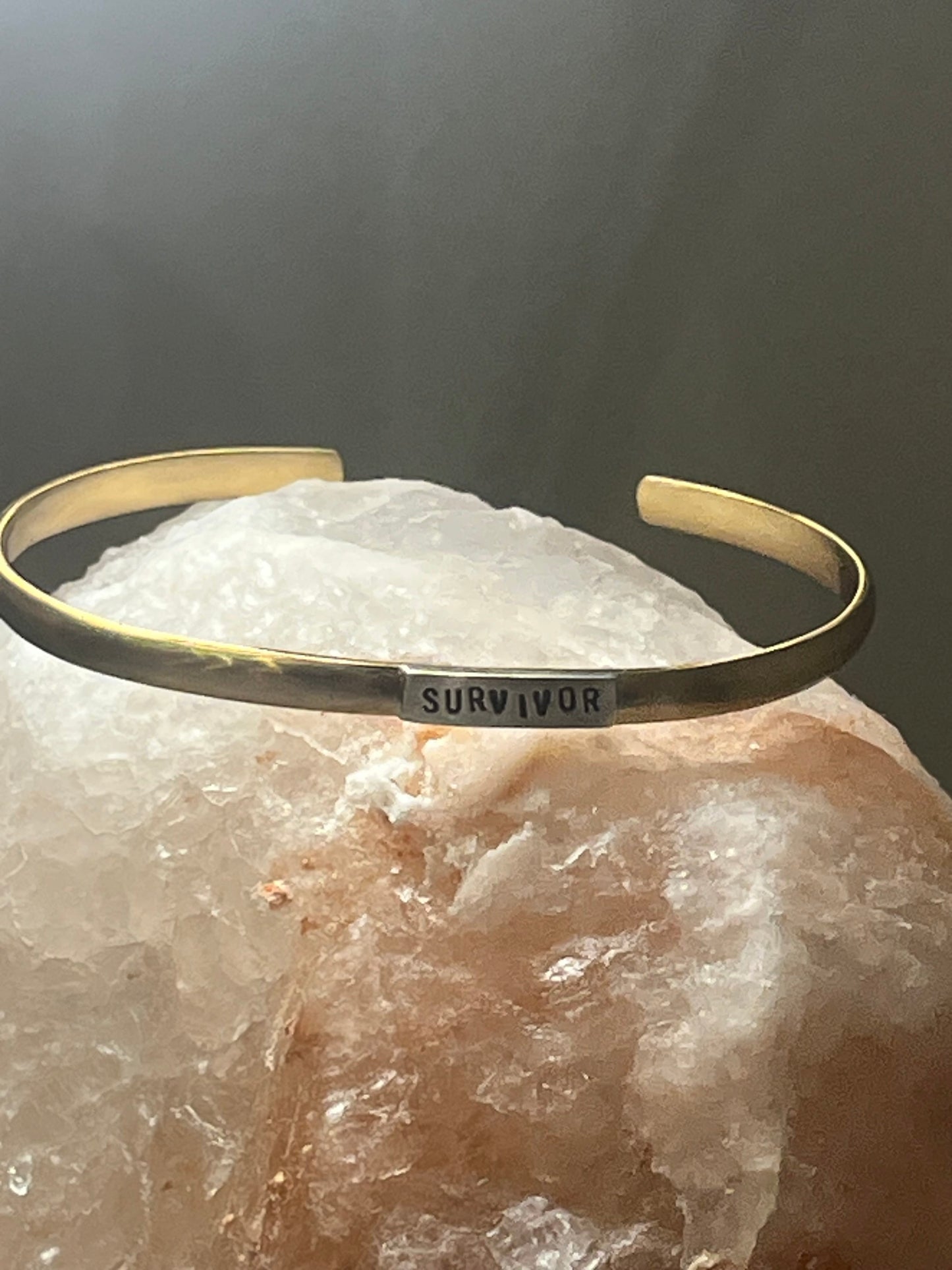 Gold bracelet with 'SURVIVOR' engraving on a crystal background