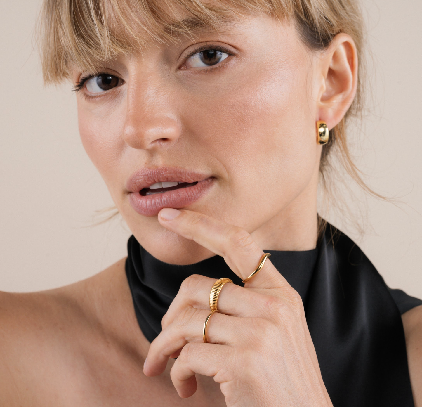 Close-up of a woman wearing gold earrings and rings against a neutral background