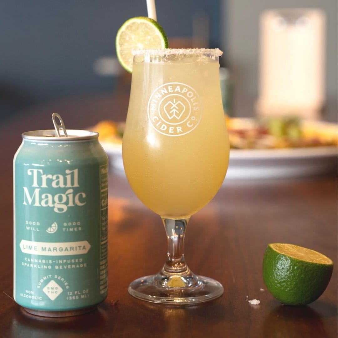 Trail Magic can and glass of lime margarita with lime garnish on a wooden surface.