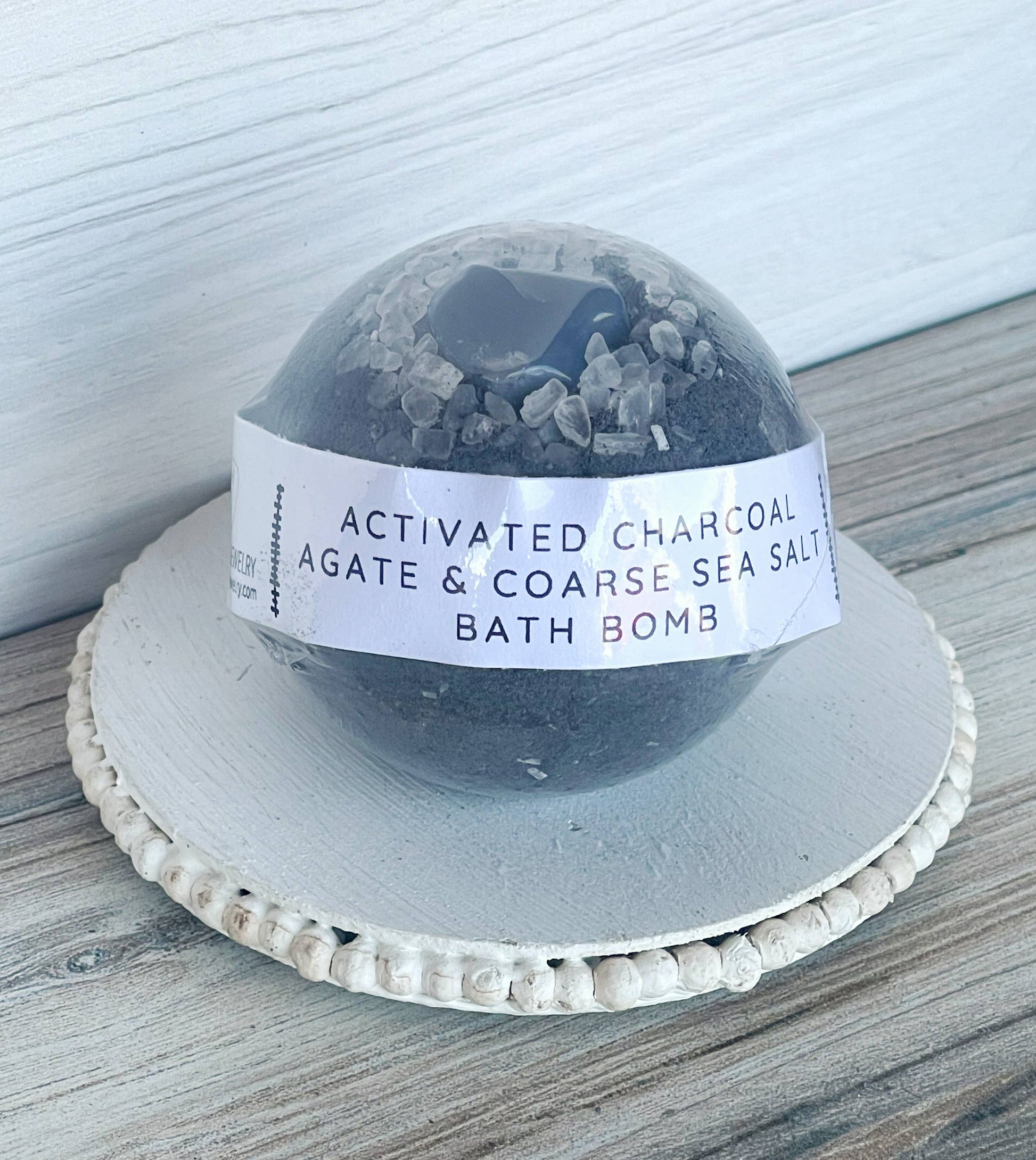 Bath bomb labeled 'Activated Charcoal Agate & Coarse Sea Salt' on a wooden surface.