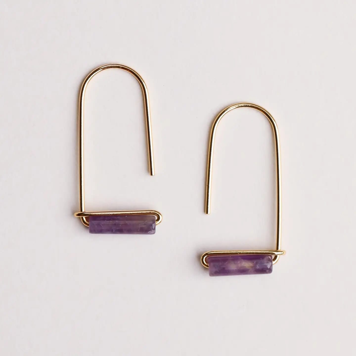 Gold earrings with purple stones on a light gray background