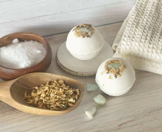 Bath bombs with gold flakes, a wooden scoop with bath salts, and a towel on a wooden surface.