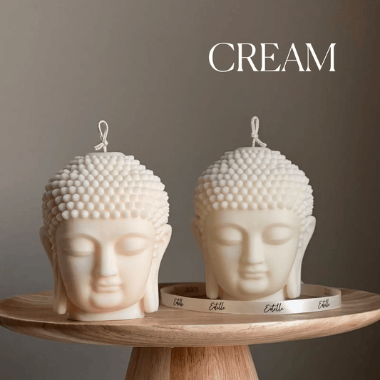 Two cream-colored Buddha head candles on a wooden stand with a neutral background.