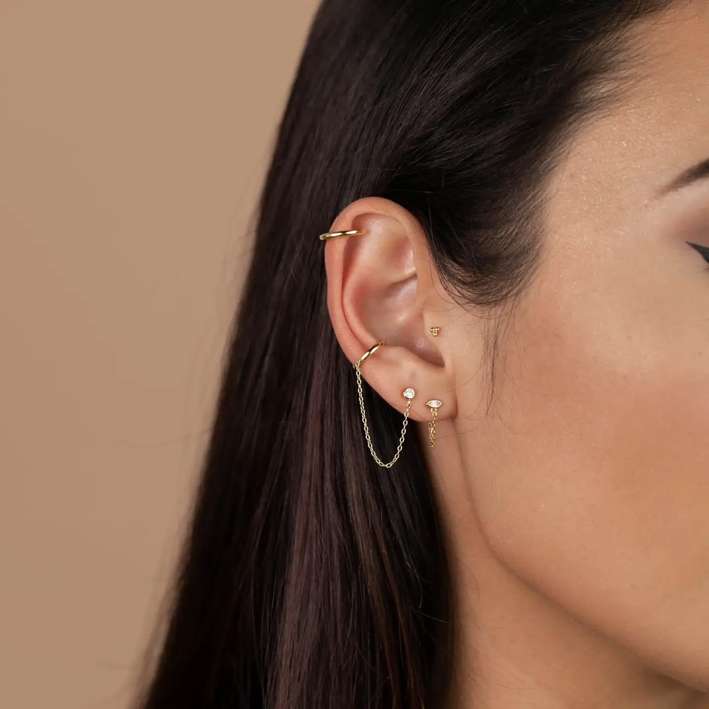 Close-up of an ear with multiple gold earrings against a beige background