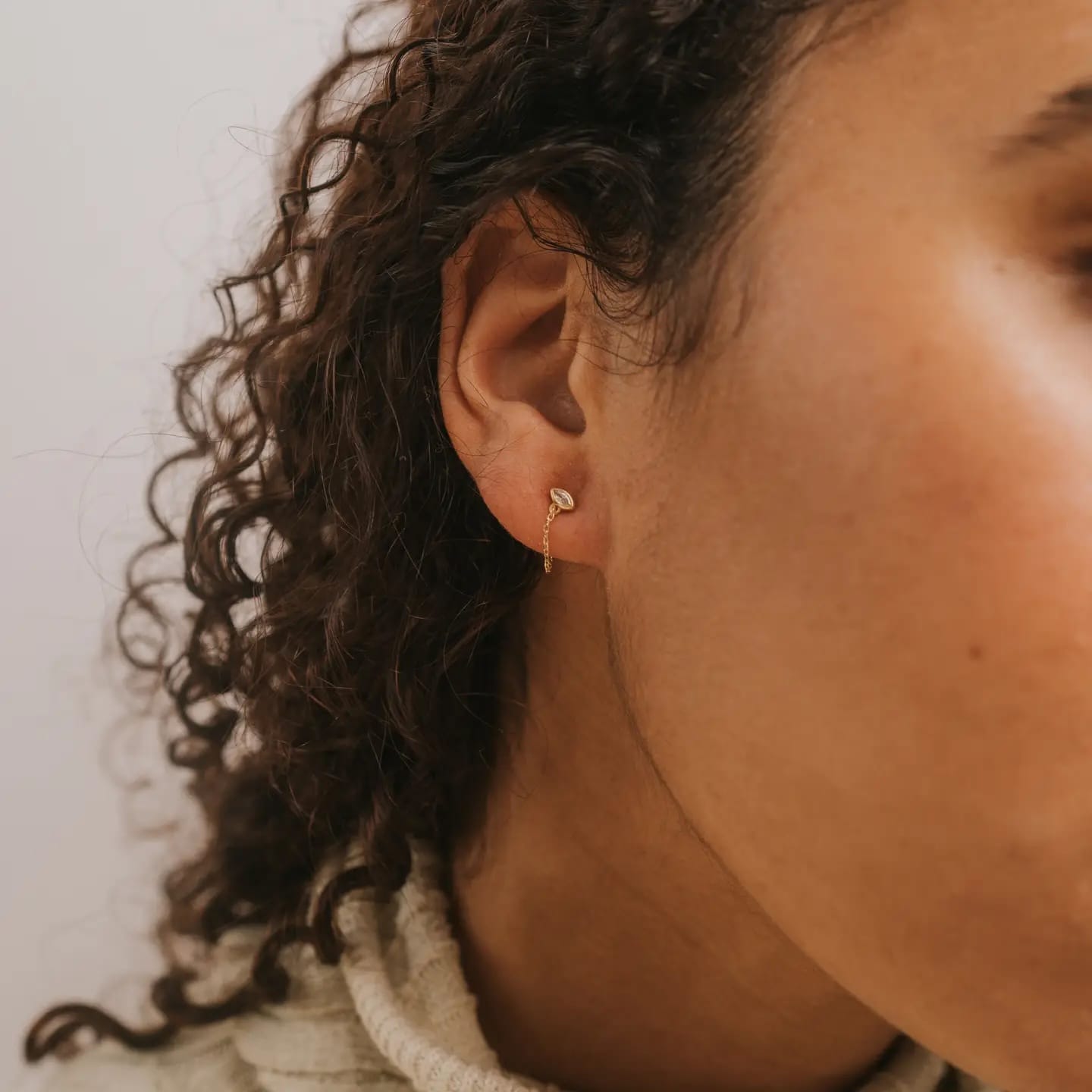 Close-up of a person wearing a gold earring with a neutral background