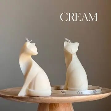 Two cat-shaped candles on a wooden stand with 'CREAM' text above.