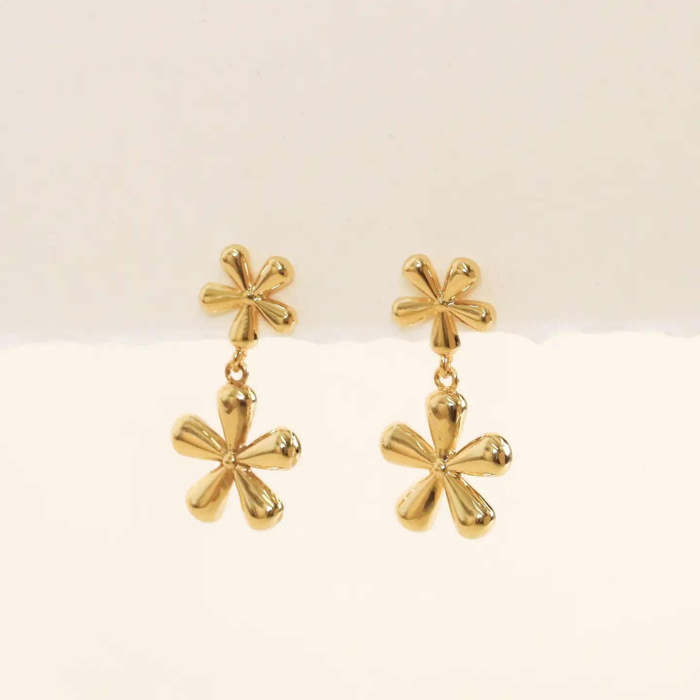 Pair of gold floral earrings on a light beige background