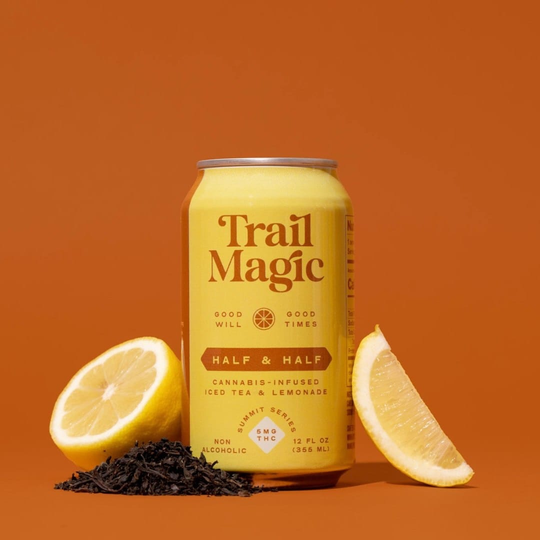 Trail Magic cannabis-infused iced tea & lemonade can with lemons and tea leaves on an orange background