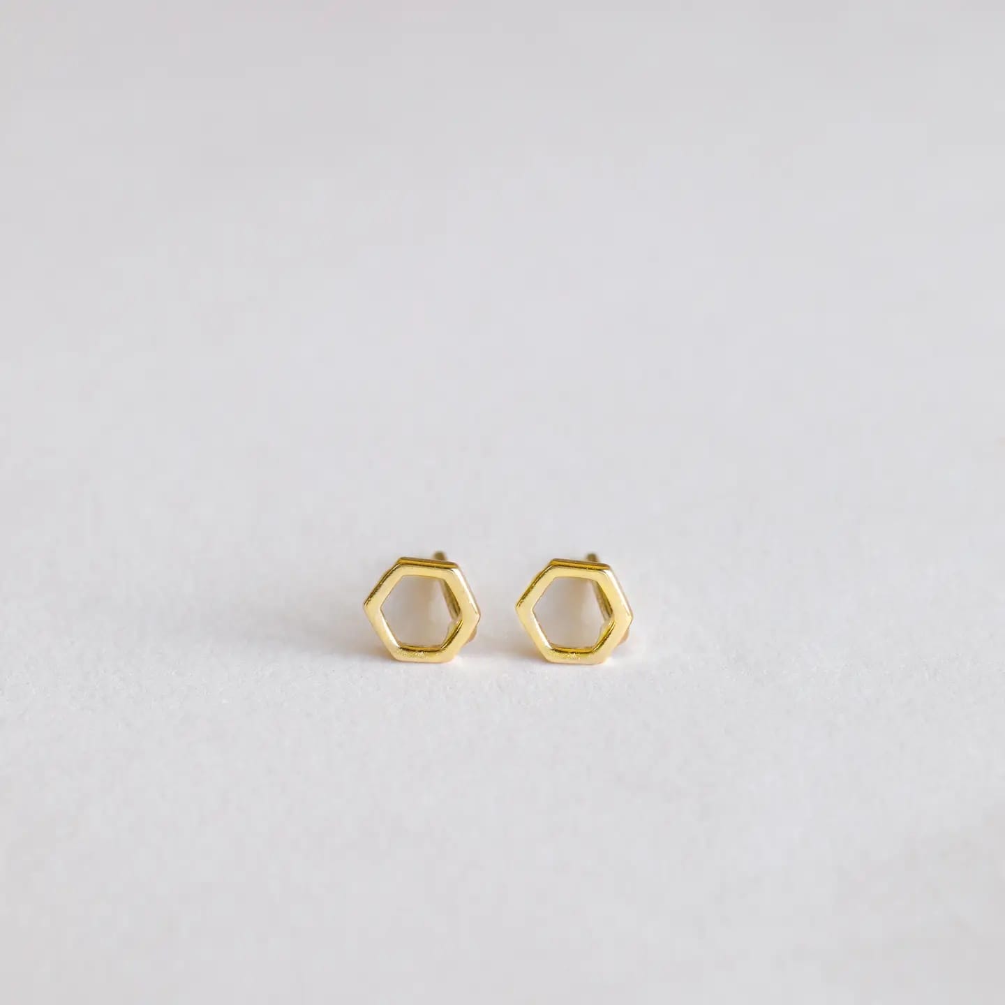 Gold hexagonal stud earrings on a light gray background