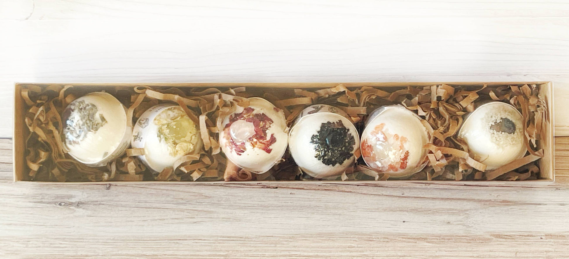 Set of six decorative bath bombs in a wooden box on a light wooden surface.