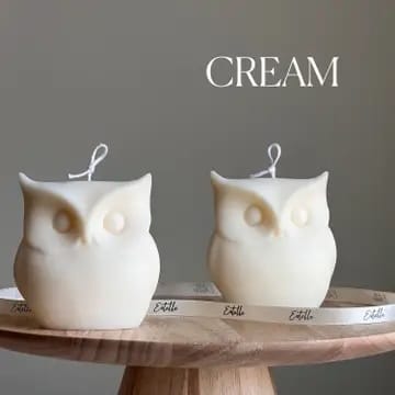 Two owl-shaped candles on a wooden surface with 'CREAM' text above.