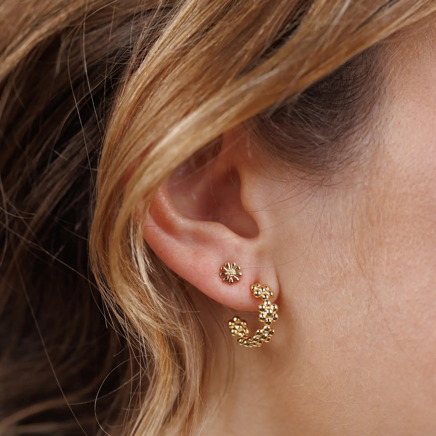 Close-up of an ear wearing gold hoop earrings and small stud daisy earrings