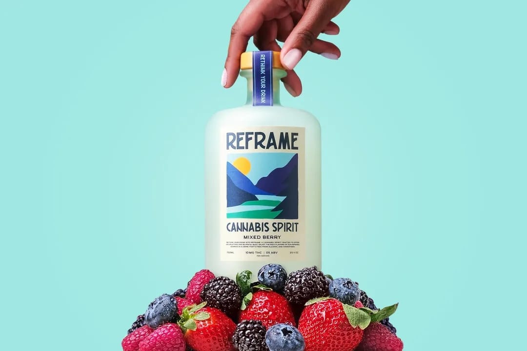 Bottle of Reframe Cannabis Spirit with a hand holding it, surrounded by berries, THC drink