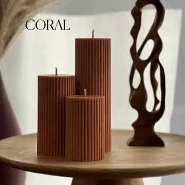 Three ribbed coral-colored candles on a wooden table with a decorative wooden sculpture.