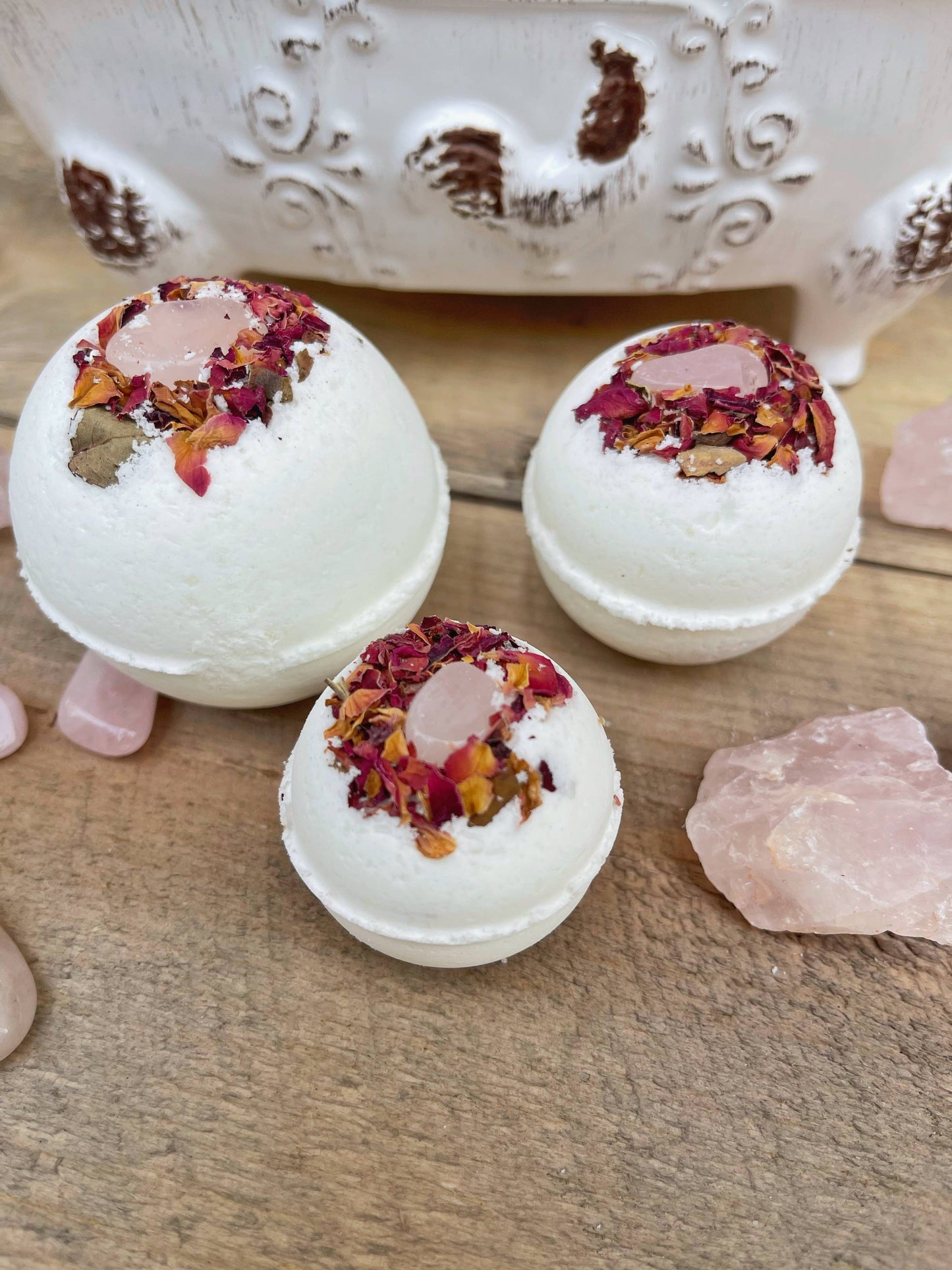 Bath bombs with rose petals on a wooden surface with a decorative container in the background.