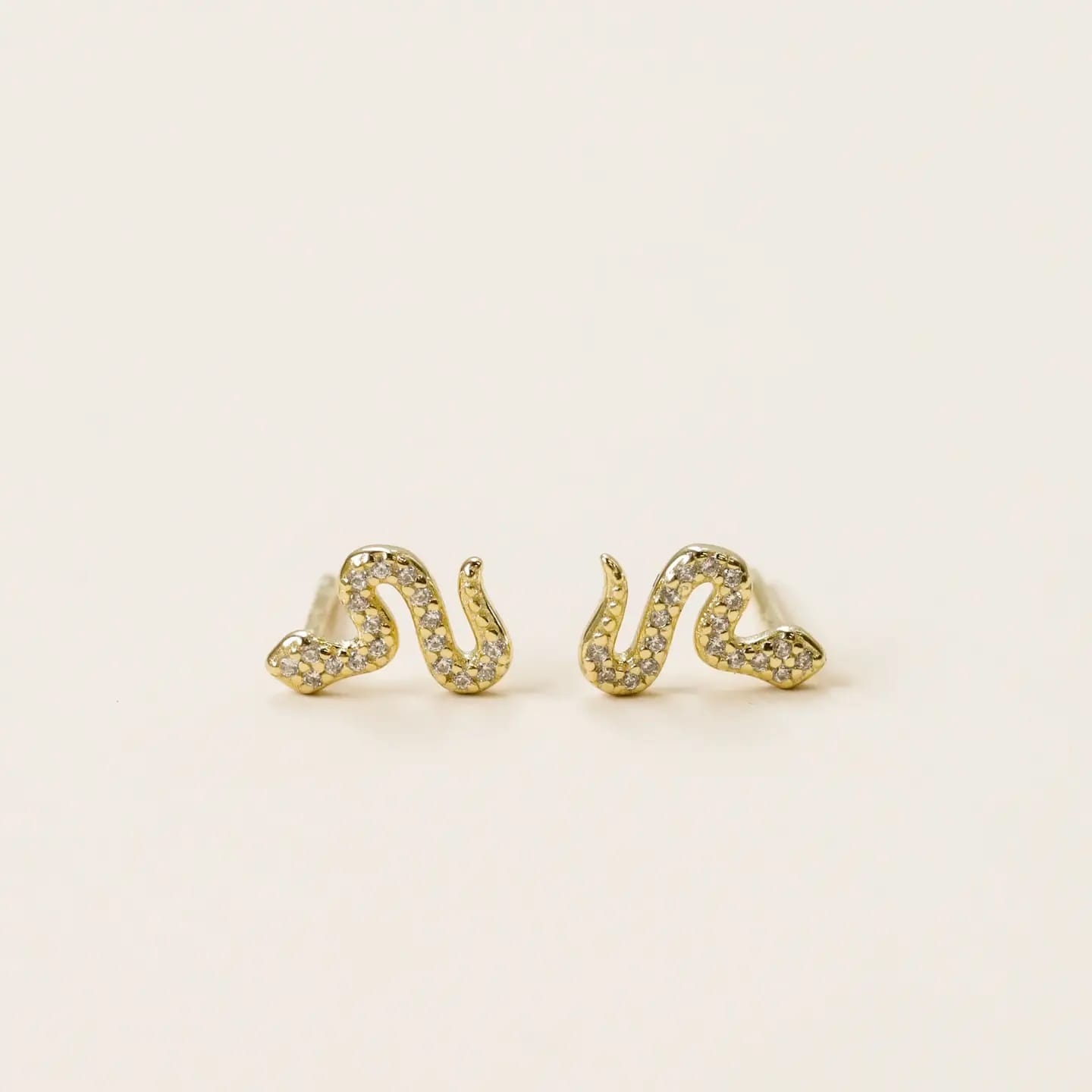 Gold snake-shaped earrings on a light beige background