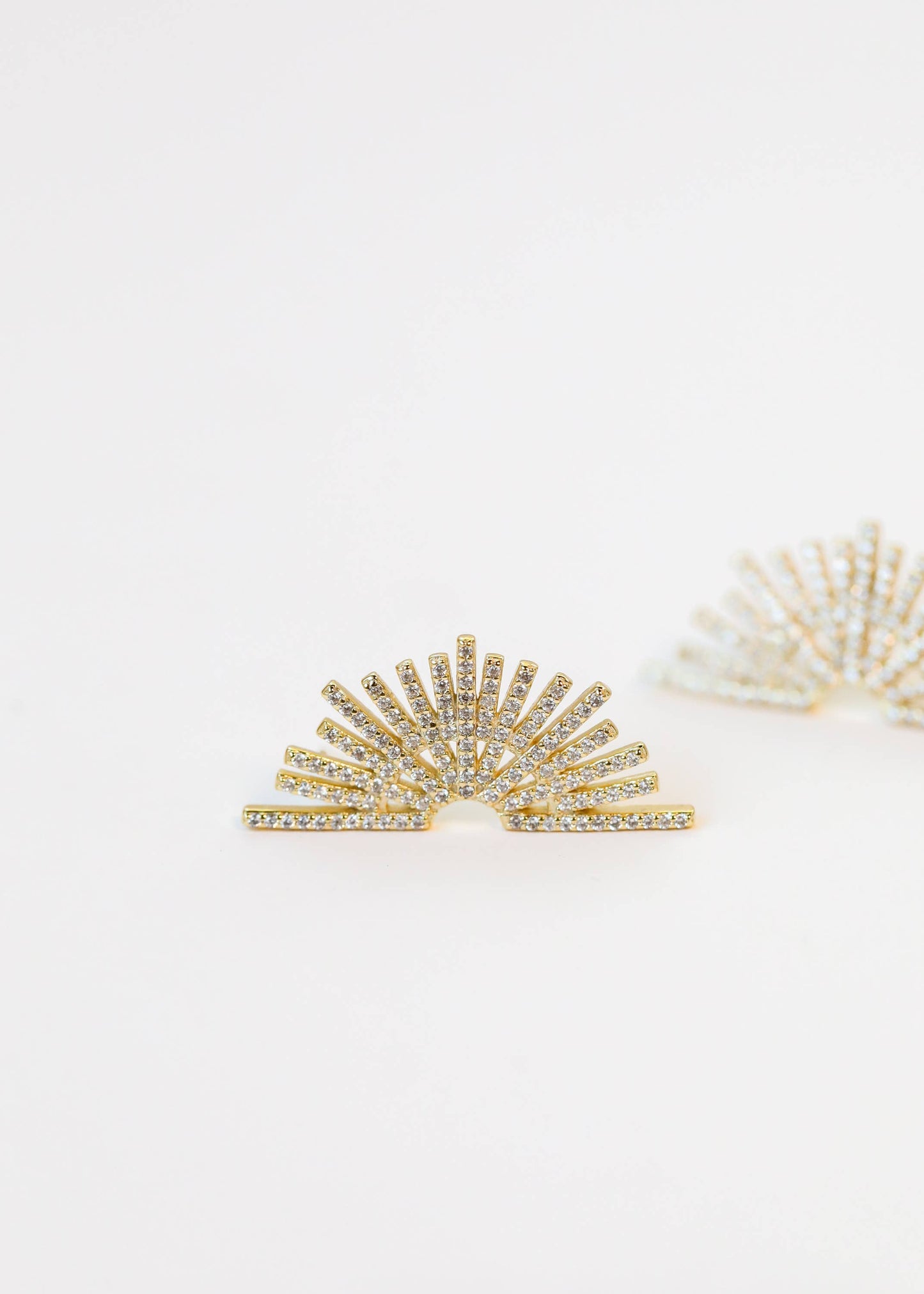 Gold sunburst earrings on a light beige background