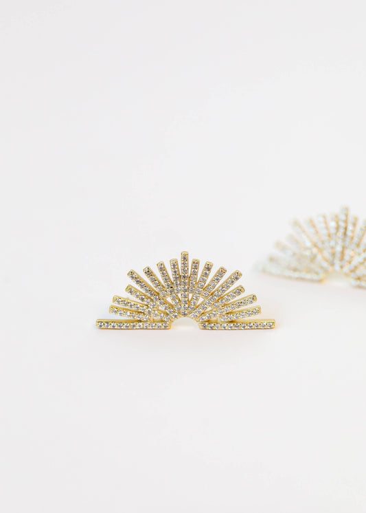 Gold sunburst earrings on a light beige background