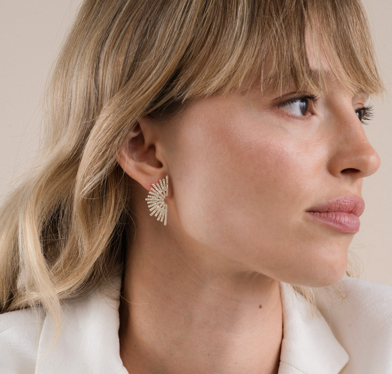 Close-up of a woman wearing gold earrings with a neutral background