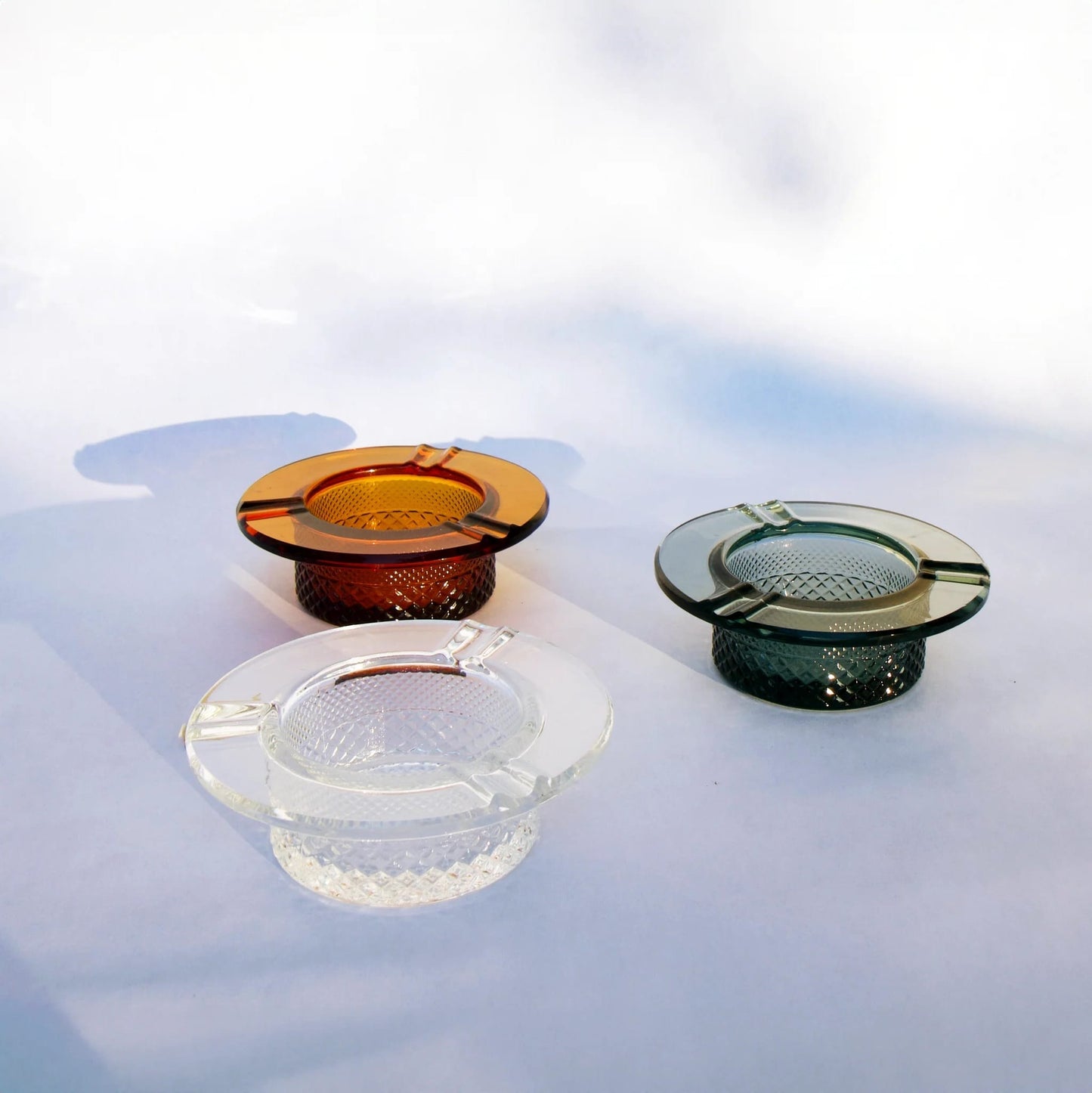 Four glass ashtrays in different colors on a light background