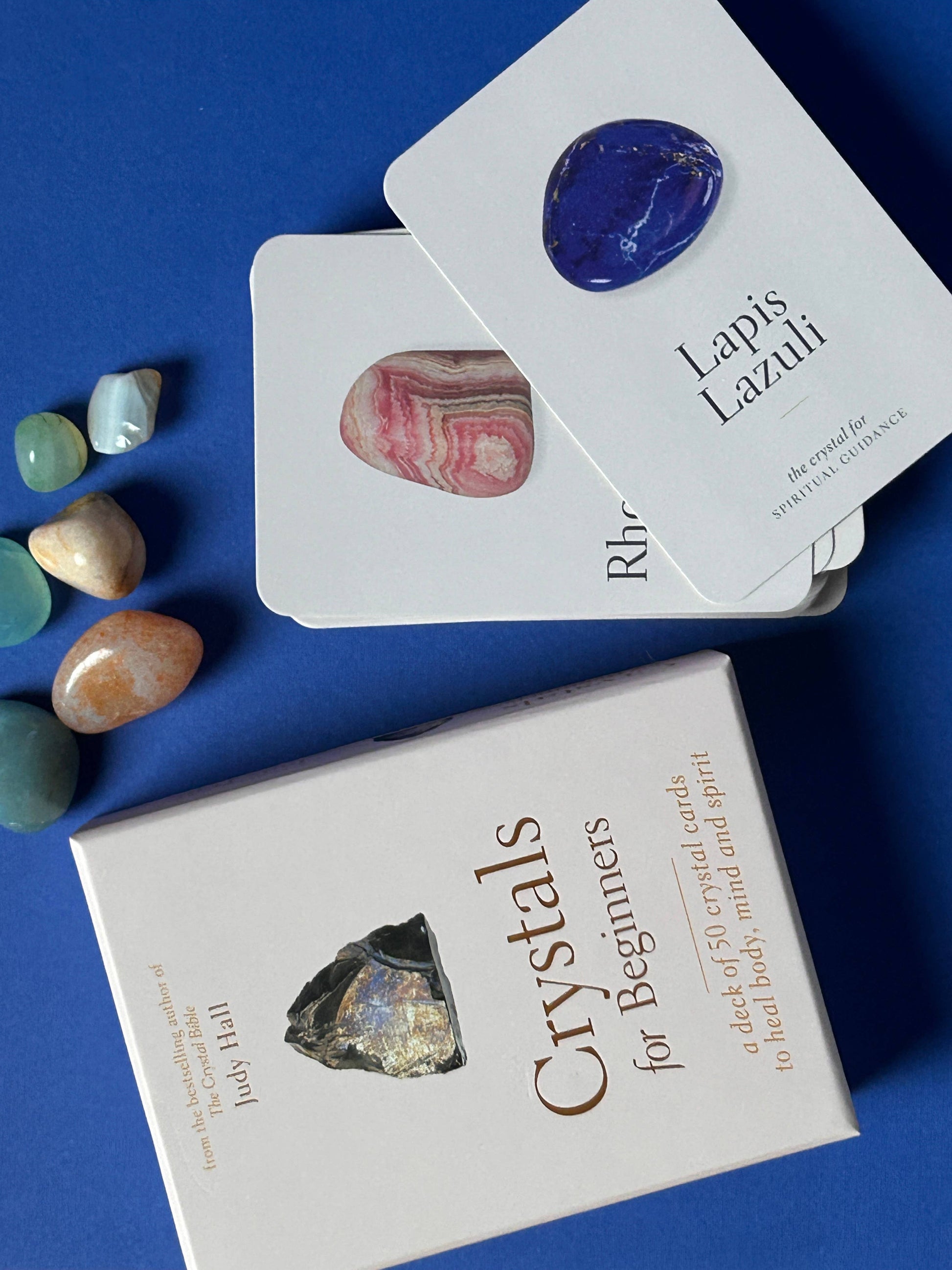 Two crystal card decks on a blue background with colorful stones around them.