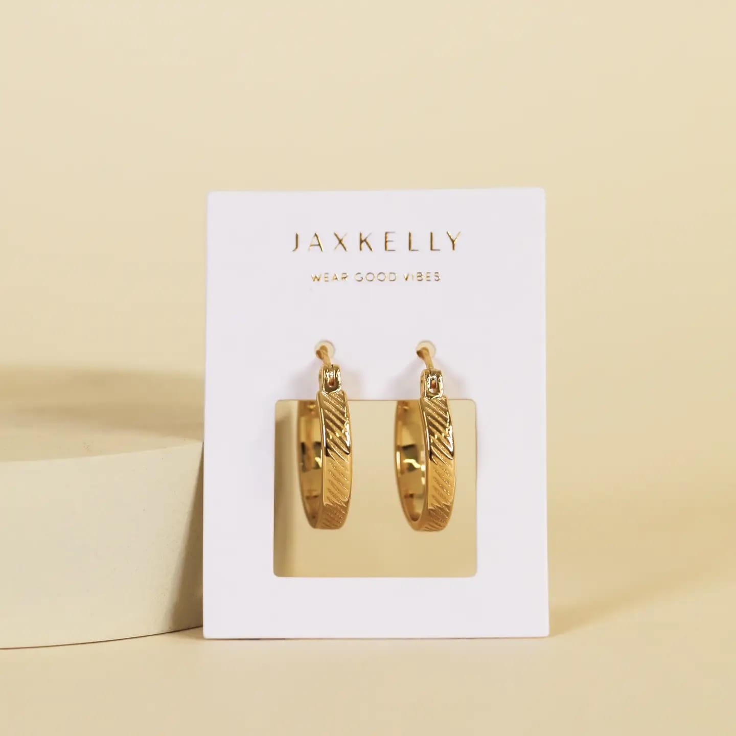 Gold hoop earrings on a Jaxkelly branded card against a beige background
