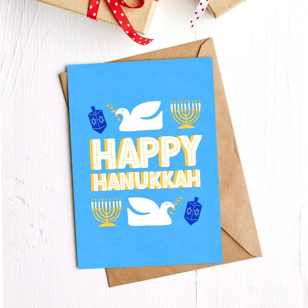 Hanukkah card with blue background and festive symbols, placed on a white surface.
