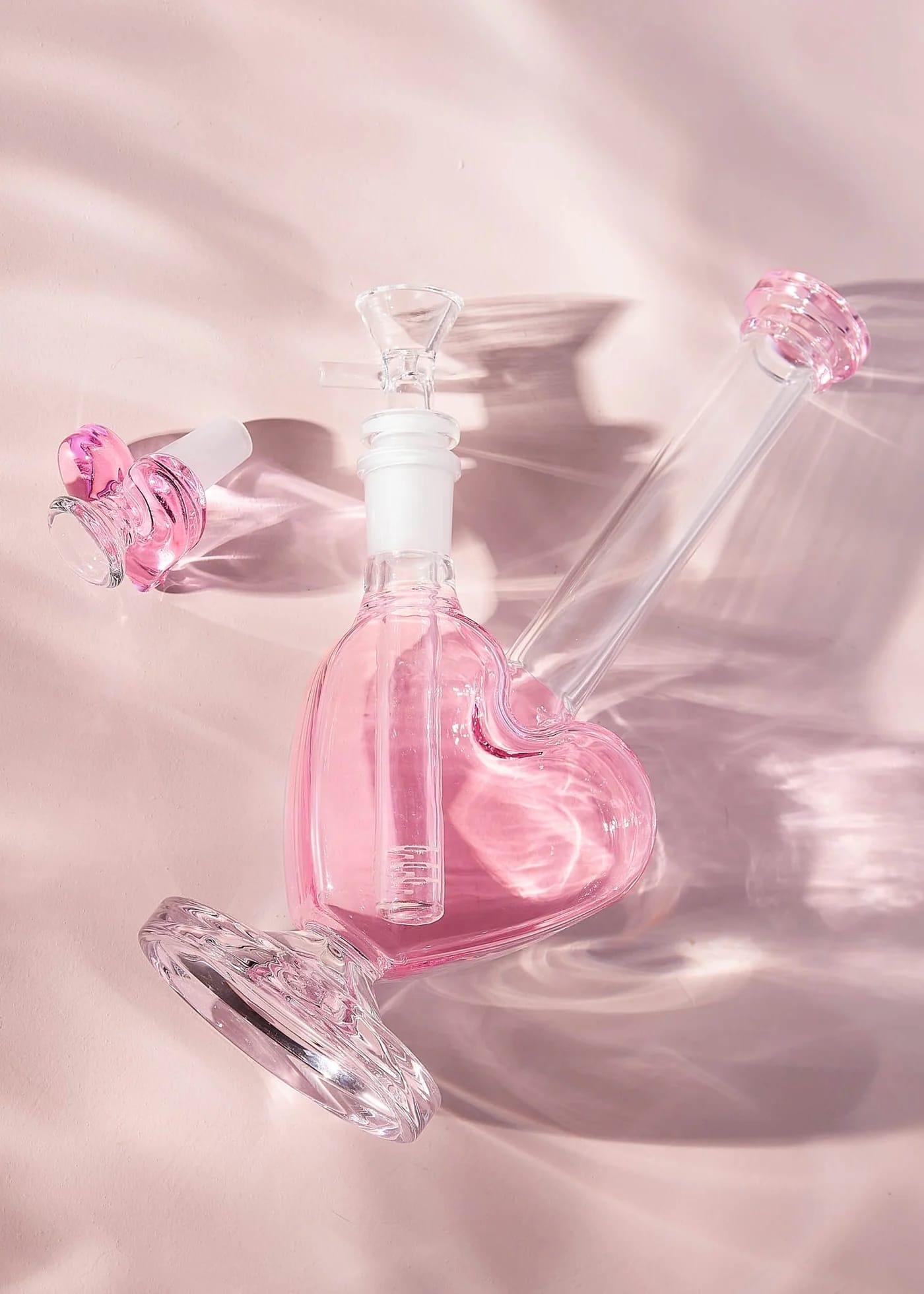 Heart-shaped pink and clear glass bottle on a reflective pink surface
