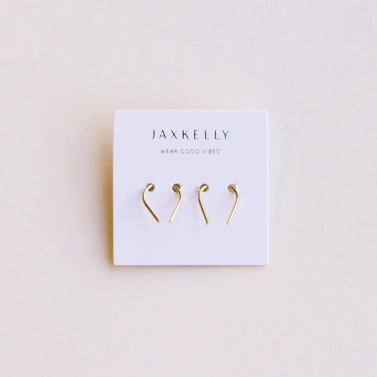 Gold earrings on a Jaxkelly branded card against a beige background