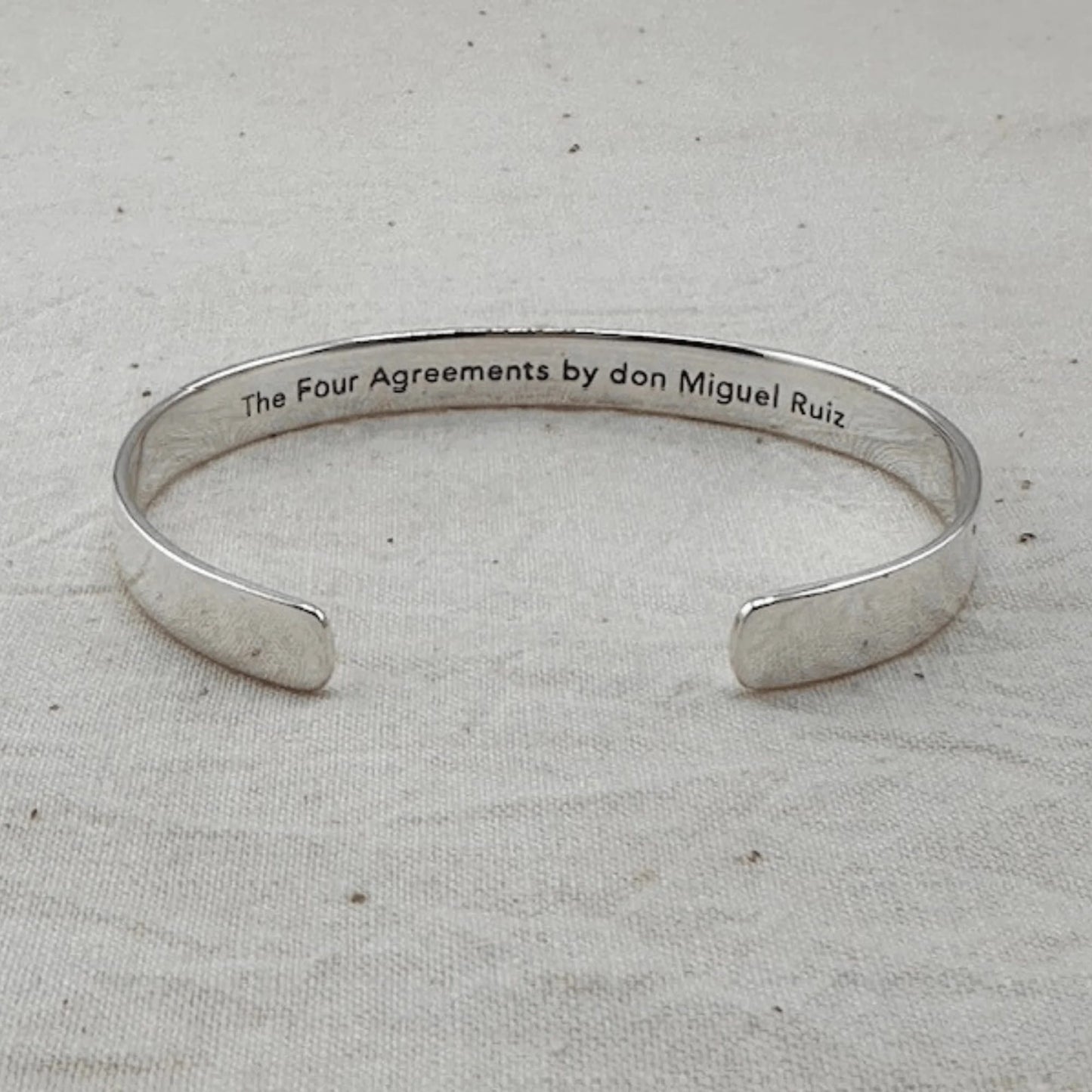 Silver bracelet with 'The Four Agreements by don Miguel Ruiz' text on a light gray background