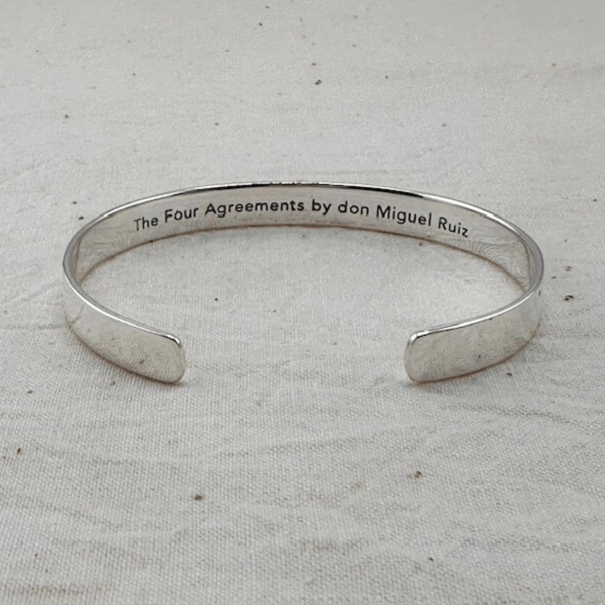 Silver bracelet with 'The Four Agreements by don Miguel Ruiz' text on a light gray background