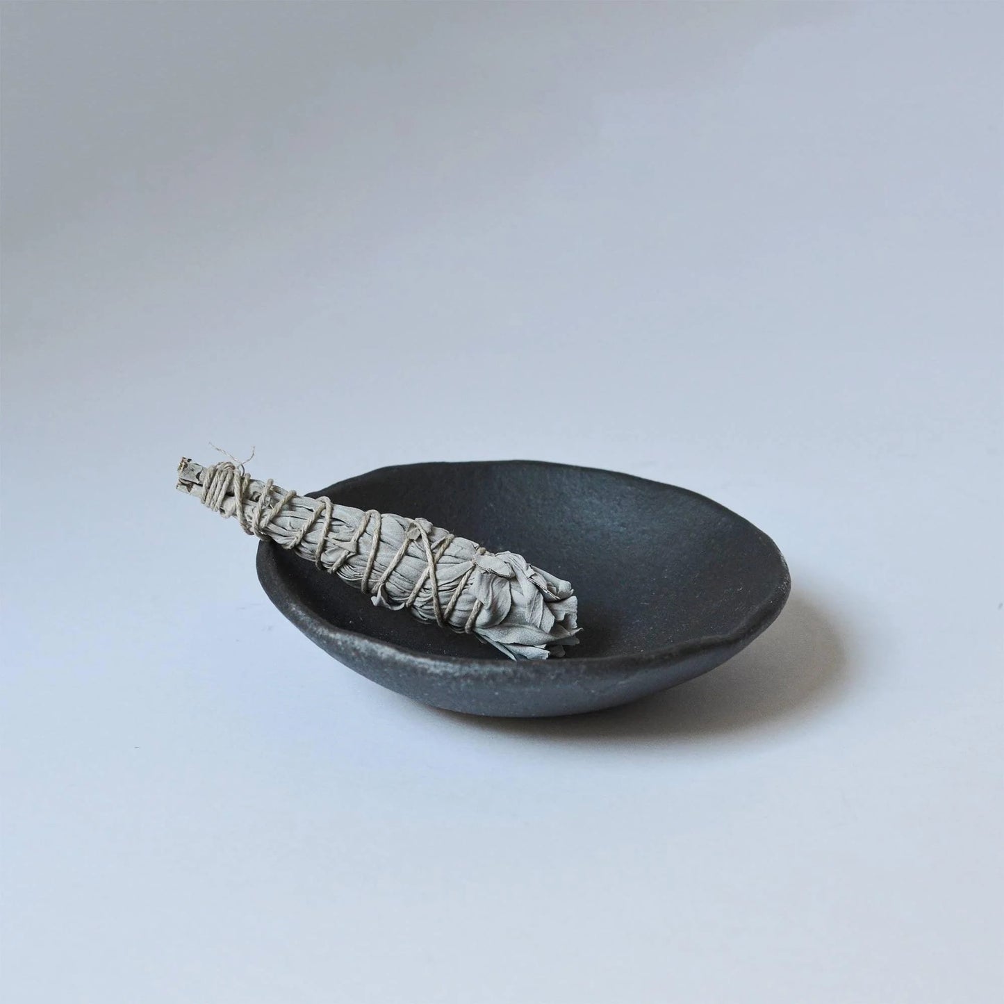 Woven sage bundle in a black ceramic dish on a light gray background