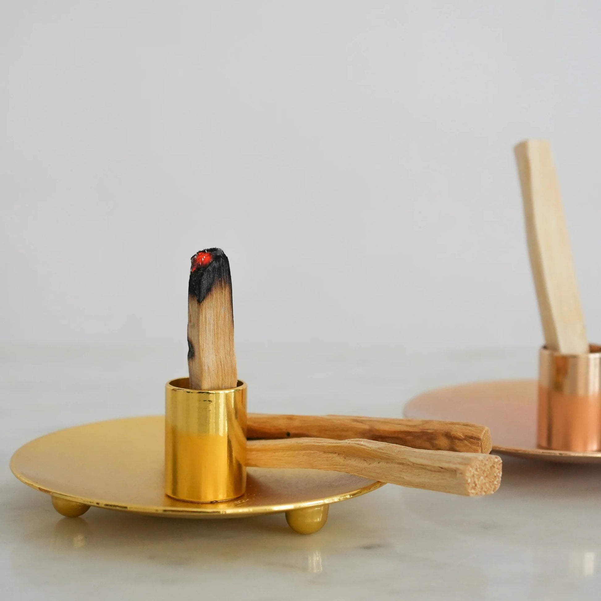 Palo Santo stick resting in a gold holder with ashes collected neatly below.