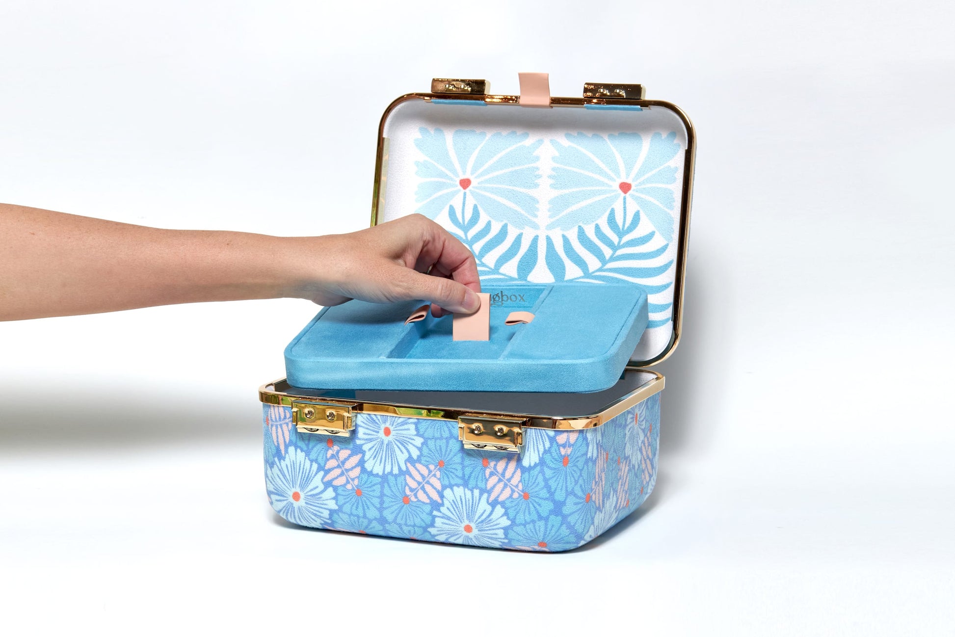 Blue floral-patterned jewelry box with a hand opening it on a white background