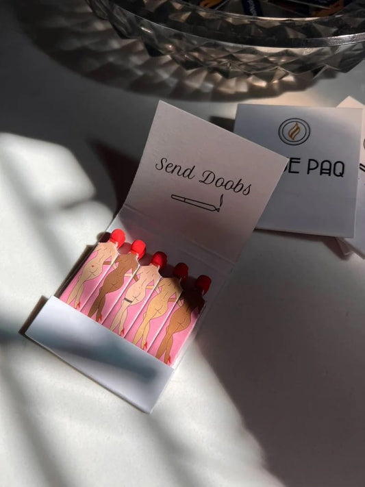 Matchbox with illustrations of women and red matches, labeled 'Send Doobs', on a white surface.