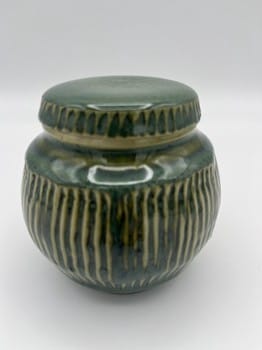 Green ceramic jar with ribbed texture on a white background