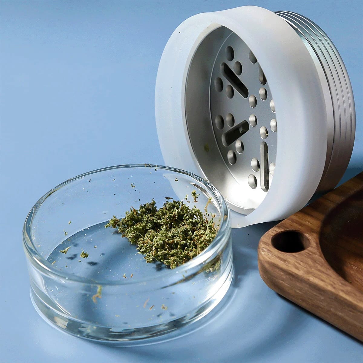 Glass container with cannabis buds next to a white grinder on a blue background