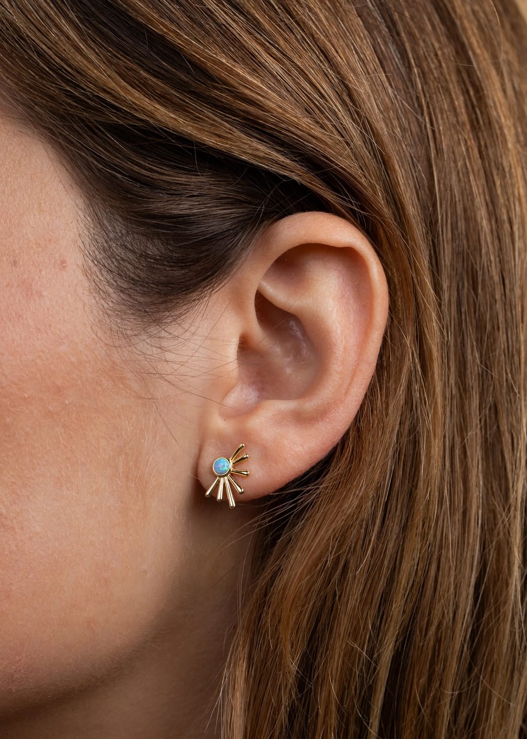 Close-up of an ear wearing a gold earring with a blue gemstone.